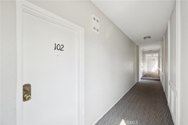 hall featuring dark colored carpet, visible vents, and baseboards