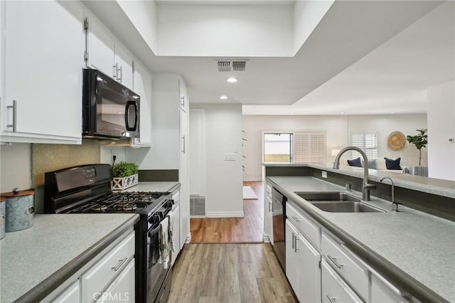 kitchen featuring visible vents, white cabinets, a sink, light wood-type flooring, and black appliances