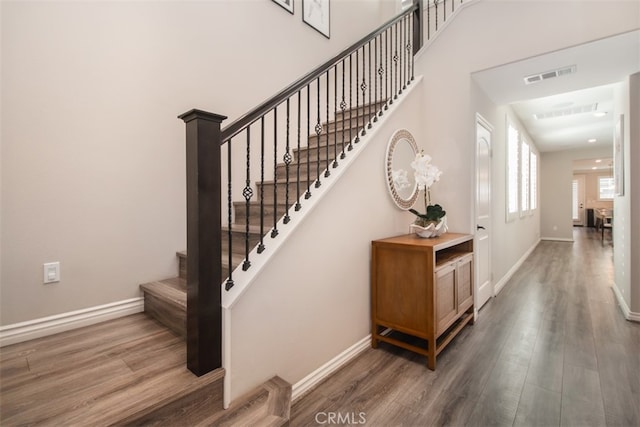 stairway with baseboards, a high ceiling, visible vents, and wood finished floors