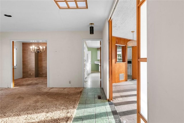 hallway with carpet, visible vents, wood walls, and a notable chandelier