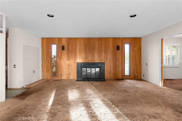 unfurnished living room with wooden walls, carpet flooring, and a tile fireplace