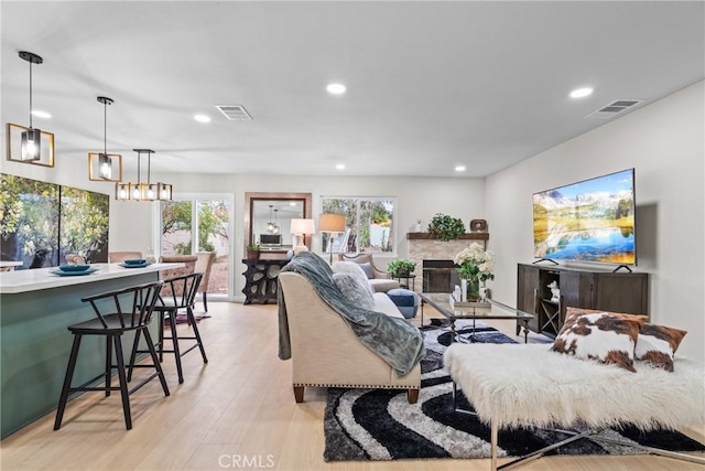 living room featuring a stone fireplace, recessed lighting, visible vents, and light wood finished floors