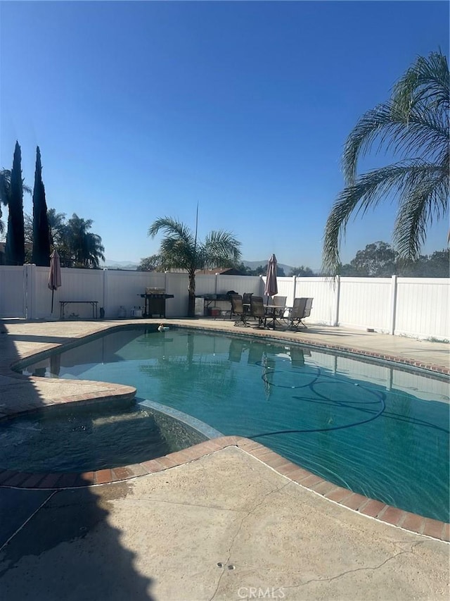 view of swimming pool featuring a fenced backyard, a pool with connected hot tub, and a patio