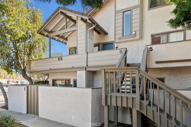 view of front of house with stairs, fence, a tile roof, and stucco siding