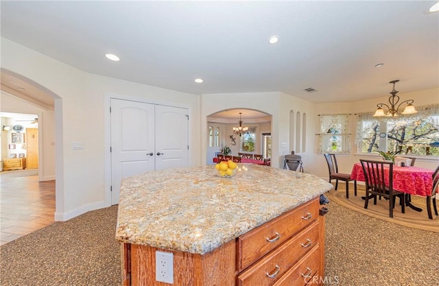 kitchen featuring arched walkways, light stone counters, a center island, a notable chandelier, and recessed lighting