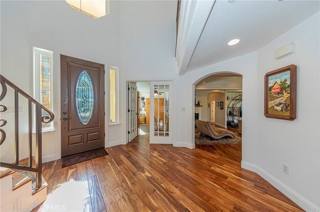 foyer featuring arched walkways, stairway, baseboards, and wood finished floors