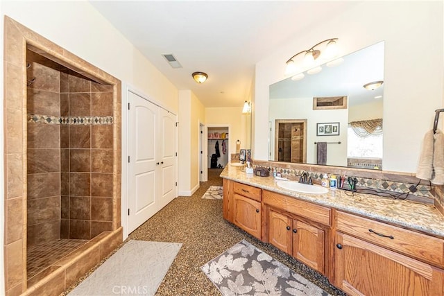 full bathroom featuring vanity, a tile shower, visible vents, and a walk in closet