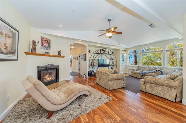 living room featuring arched walkways, wood finished floors, baseboards, vaulted ceiling, and a glass covered fireplace