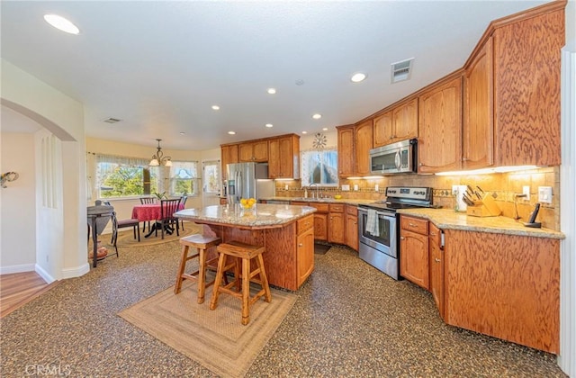 kitchen with stainless steel appliances, a kitchen island, a sink, visible vents, and backsplash