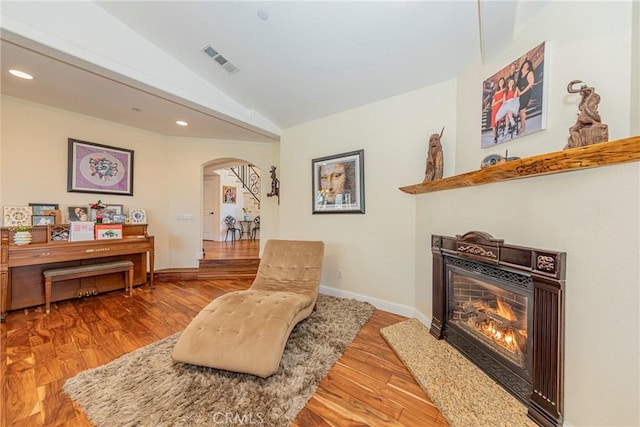 sitting room featuring arched walkways, visible vents, vaulted ceiling, wood finished floors, and a lit fireplace