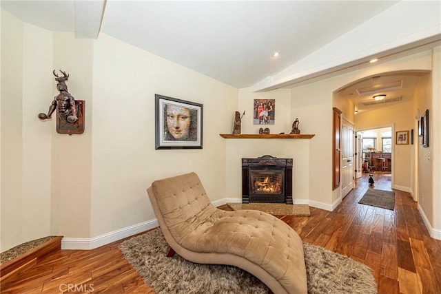 sitting room featuring lofted ceiling, arched walkways, baseboards, and wood finished floors