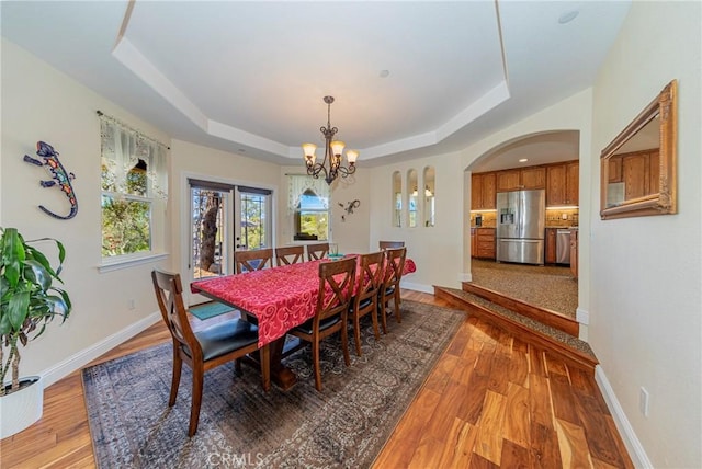 dining room with arched walkways, a raised ceiling, and wood finished floors