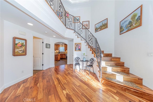 interior space with arched walkways, a high ceiling, baseboards, and wood finished floors