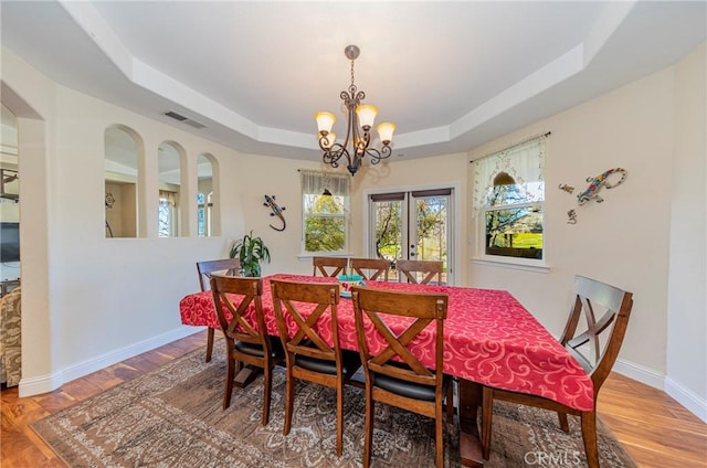 dining room with visible vents, a tray ceiling, wood finished floors, and french doors