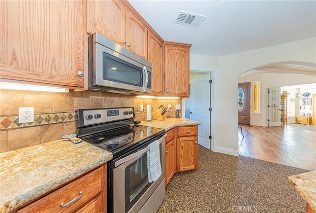 kitchen with arched walkways, visible vents, baseboards, appliances with stainless steel finishes, and decorative backsplash