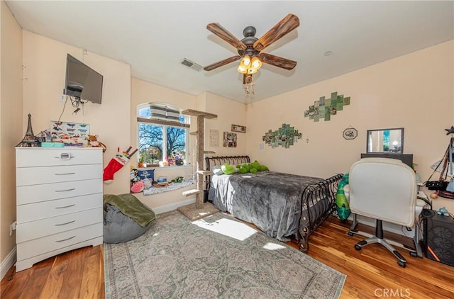 bedroom featuring a ceiling fan, wood finished floors, visible vents, and baseboards