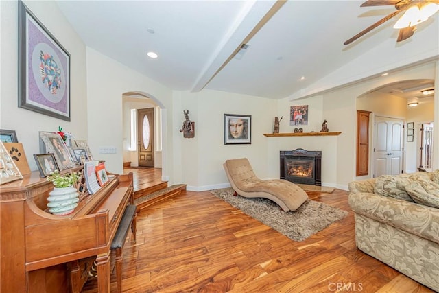 living area with arched walkways, a lit fireplace, lofted ceiling, and light wood-style flooring