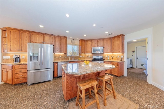 kitchen with appliances with stainless steel finishes, backsplash, washer / dryer, and a center island