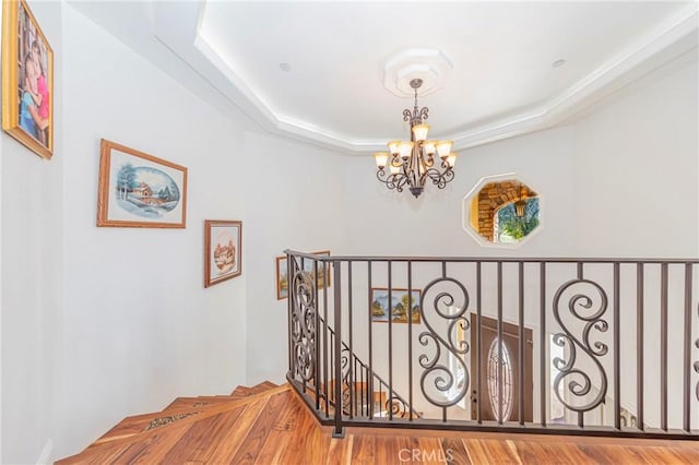 corridor featuring a raised ceiling, an upstairs landing, and an inviting chandelier