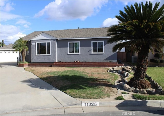 ranch-style house featuring cooling unit, roof with shingles, a front lawn, and stucco siding