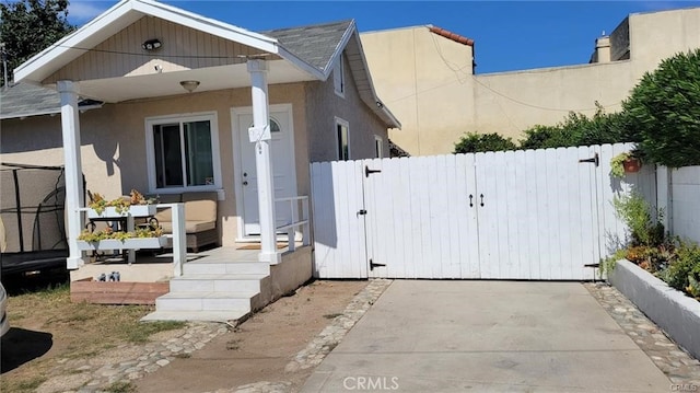 view of front of home with covered porch, fence, a gate, and stucco siding