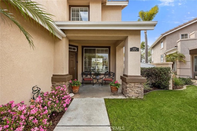 view of exterior entry with a lawn and stucco siding