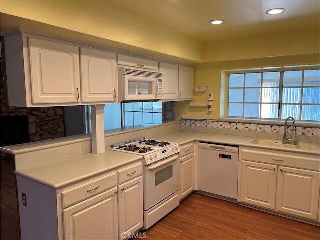 kitchen featuring wood finished floors, white appliances, a sink, and white cabinets