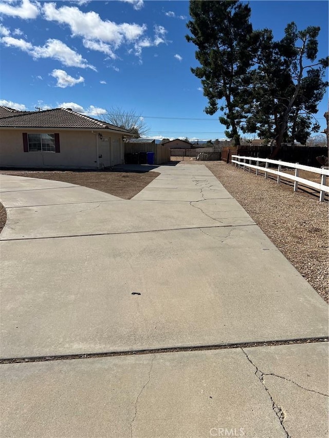 view of side of property with driveway, stucco siding, fence, and a tiled roof