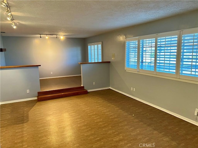 empty room featuring a textured ceiling, baseboards, track lighting, and wood finished floors