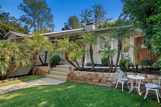 exterior space featuring a chimney, fence, a front lawn, and stucco siding