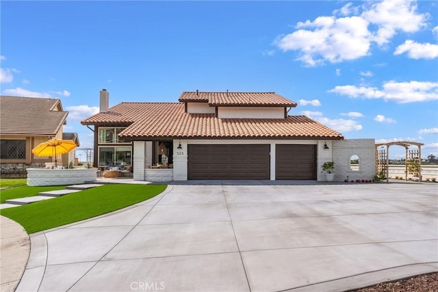 mediterranean / spanish home with a garage, concrete driveway, a tile roof, and a chimney