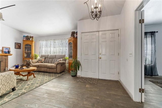 foyer featuring wood finish floors, a fireplace with raised hearth, a notable chandelier, and baseboards