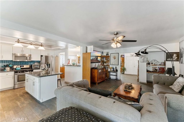 living room with a tray ceiling, a toaster, a ceiling fan, and wood finished floors