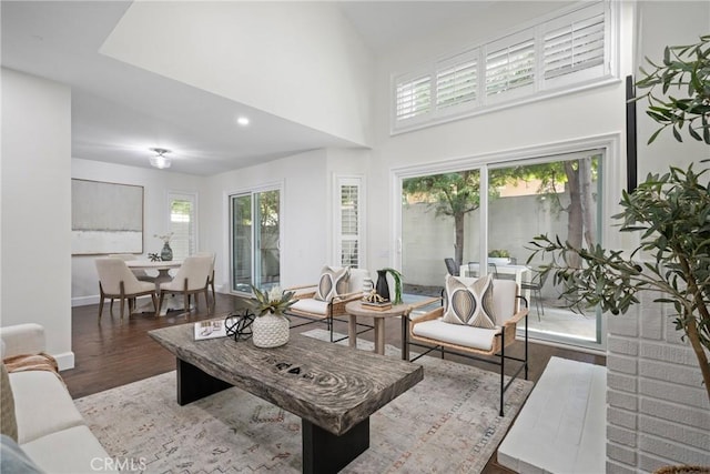 living room with plenty of natural light, a towering ceiling, baseboards, and wood finished floors