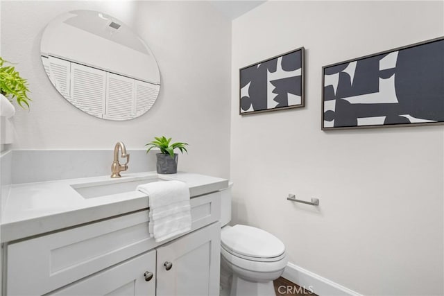 half bathroom featuring toilet, baseboards, and vanity