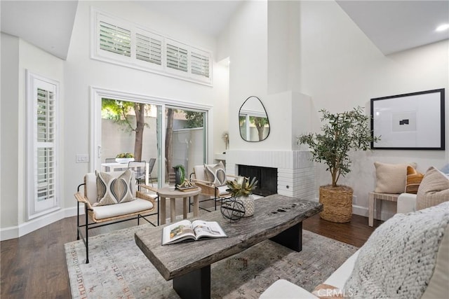 living area with a brick fireplace, a high ceiling, baseboards, and wood finished floors