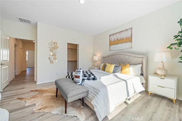 bedroom with baseboards, visible vents, a walk in closet, light wood-style floors, and a closet