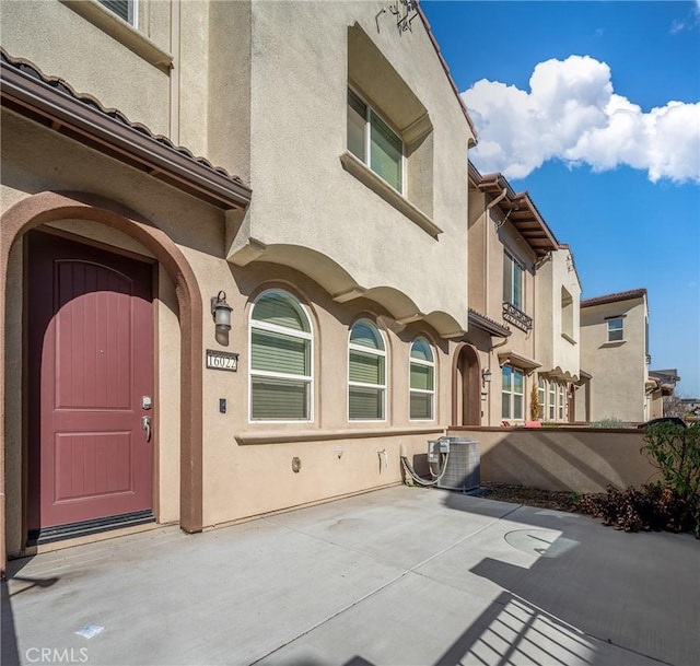 view of exterior entry featuring a patio, cooling unit, and stucco siding