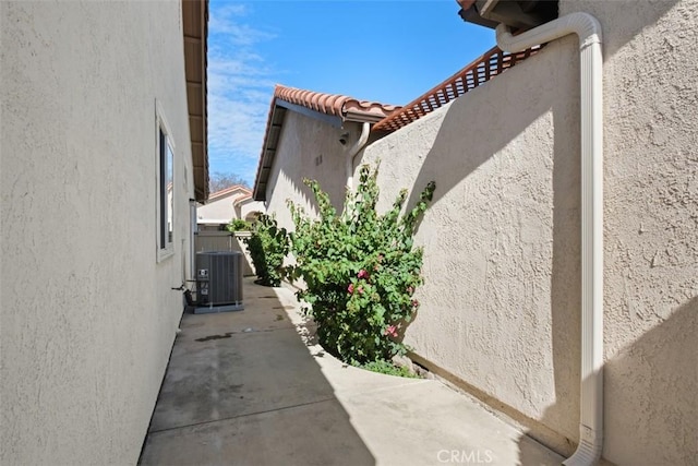 view of side of property with a tile roof, a patio area, central AC unit, and stucco siding