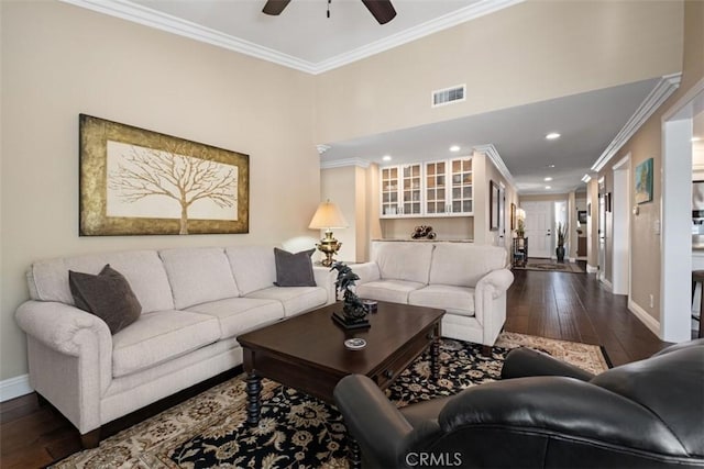 living area with dark wood finished floors, crown molding, visible vents, a ceiling fan, and baseboards