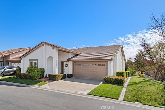 view of front facade with a front yard, concrete driveway, a tile roof, and an attached garage