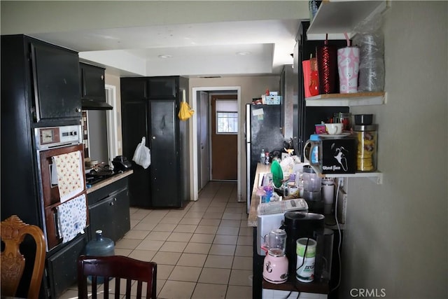 kitchen featuring a warming drawer, dark cabinetry, light tile patterned floors, freestanding refrigerator, and oven