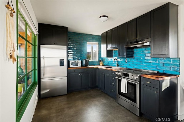 kitchen featuring under cabinet range hood, stainless steel appliances, butcher block counters, a sink, and backsplash