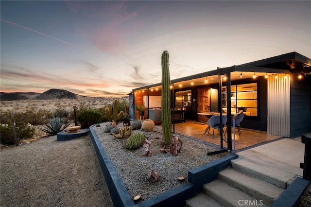 back of house at dusk with a mountain view and a patio