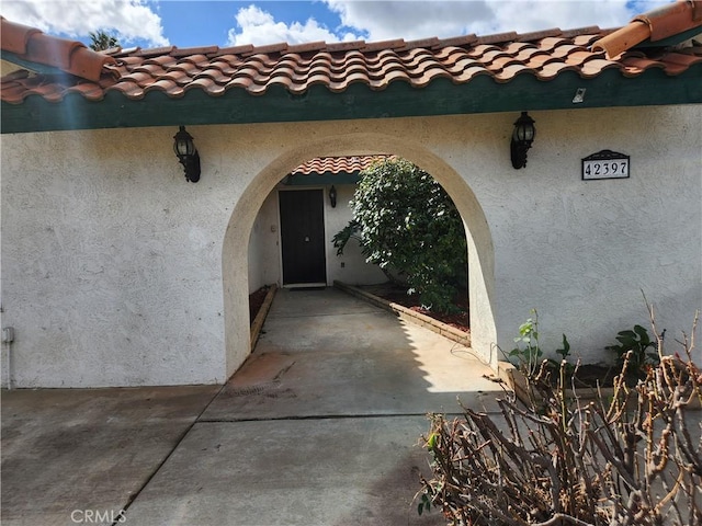 view of exterior entry with a tile roof and stucco siding