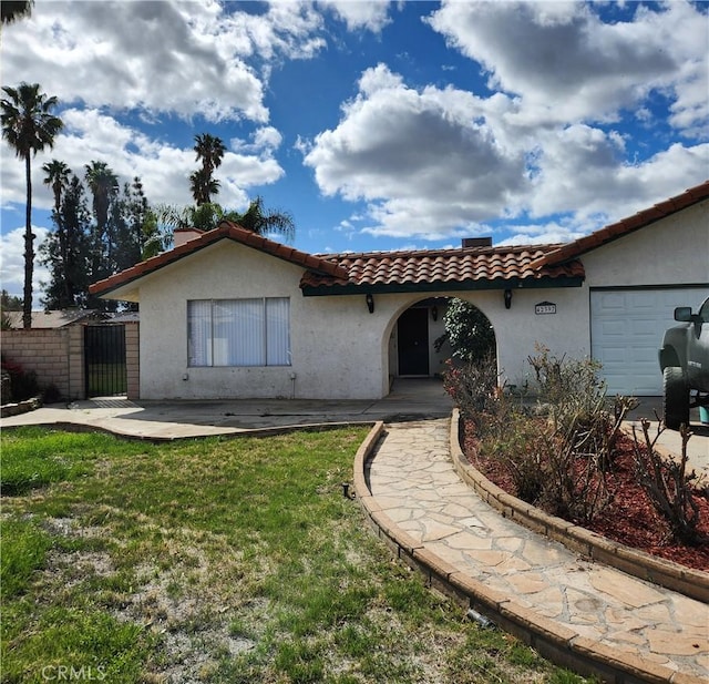 mediterranean / spanish-style home with a garage, a tiled roof, a front lawn, and stucco siding