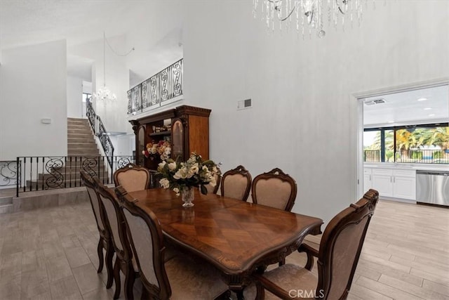 dining space with visible vents, a towering ceiling, stairway, light wood-type flooring, and a chandelier