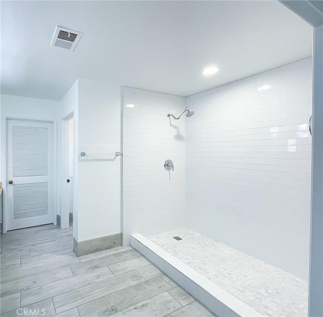 bathroom featuring wood finish floors, a tile shower, visible vents, and baseboards