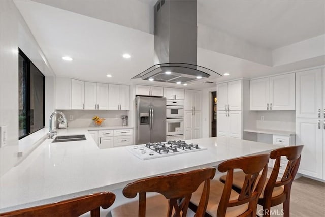 kitchen featuring white appliances, a peninsula, island exhaust hood, light countertops, and a sink