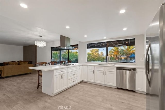 kitchen featuring a breakfast bar, island exhaust hood, stainless steel appliances, a sink, and a peninsula